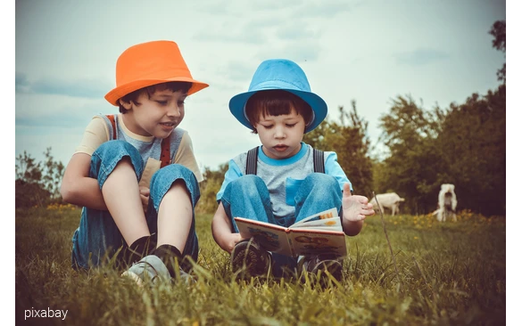 Zwei Jungen sitzen auf einer Kuhwiese und lesen in einem Buch.