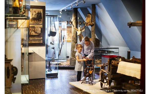 Eine Mutter und ihre Tochter betrachten eine Spindel im Südsauerlandmuseum in Attendorn.