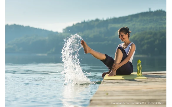Eine Frau sitzt auf einem Steg am Hennesee und spritzt mit Wasser.