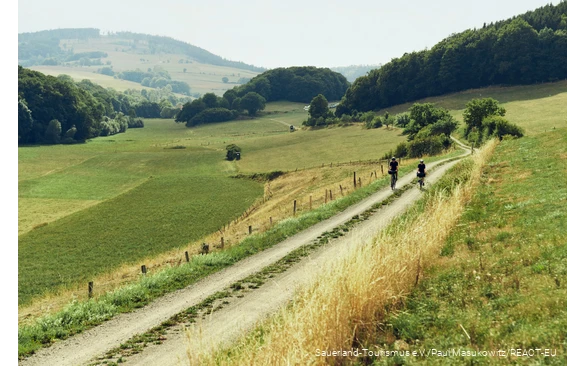 Two cyclists ride on a web through the fields along the Diemelradweg