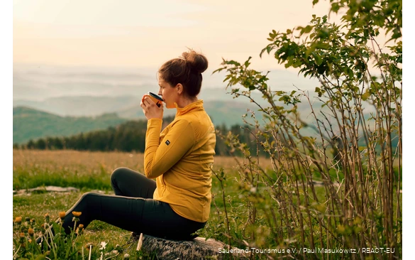 A hiker enjoys her break with a cup of coffee and a view over the landscape.