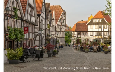 Ein Platz in Soest mit lauter Fachwerkhäusern und Menschen, die draußen in Gaststätten sitzen