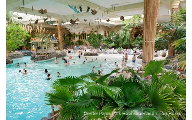 Some people swim in the Aqua Mundo adventure pool, which is decorated with numerous palm trees, making it look like a beach.