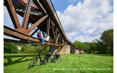 Pärchen sitzt auf dem Träger einer Brücke unter ihnen zwei E-Bikes