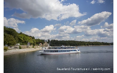 Der Möhnesee an einem Sommertag mit einem Personenschiff voller Menschen im Zentrum