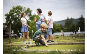 A family playing mini golf at Diemelsee. A son prepares his next shot.