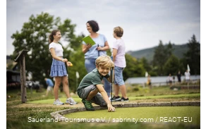 A family playing mini golf at Diemelsee. A son prepares his next shot.