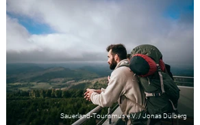 A hiker with a multi-day rucksack enjoys the view from the Bollerberg tower.