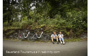 A couple of cyclists take a break at the side of the road.