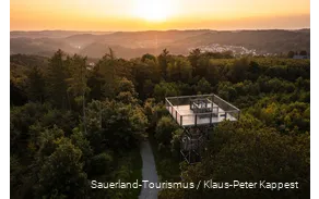Blick von oben auf den Turm. Im Hintergrund geht die Sonne unter und man sieht verschiedene Ortschaften