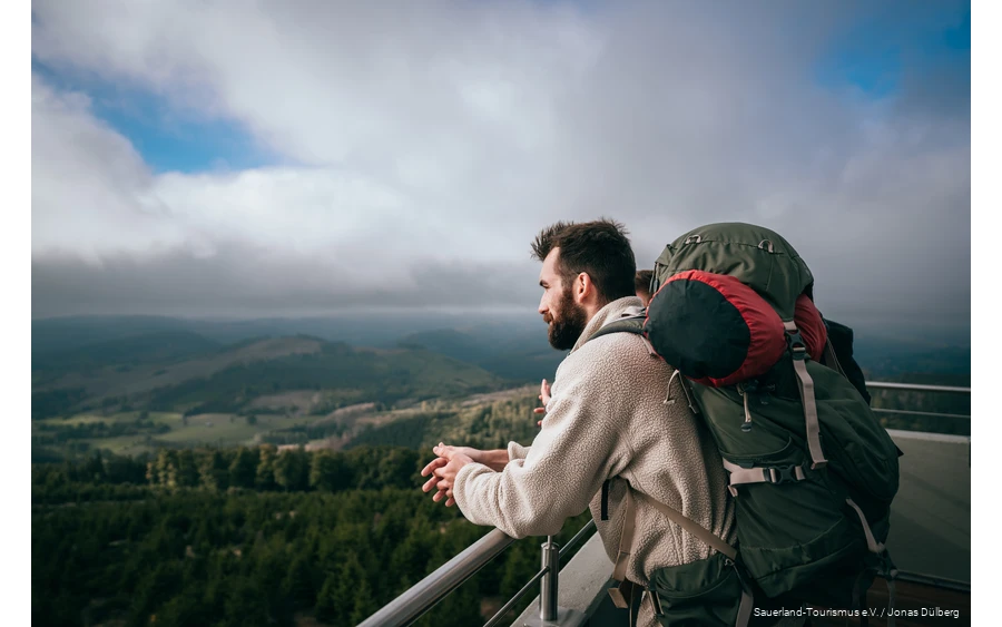 A hiker with a multi-day rucksack enjoys the view from the Bollerberg tower.
