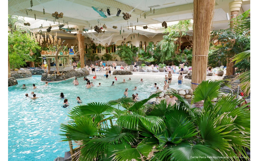 Einige Menschen baden im Erlebnisbad Aqua Mundo, das mit zahlreichen Palmen dekoriert ist, wodurch es wie ein Strand aussieht.
