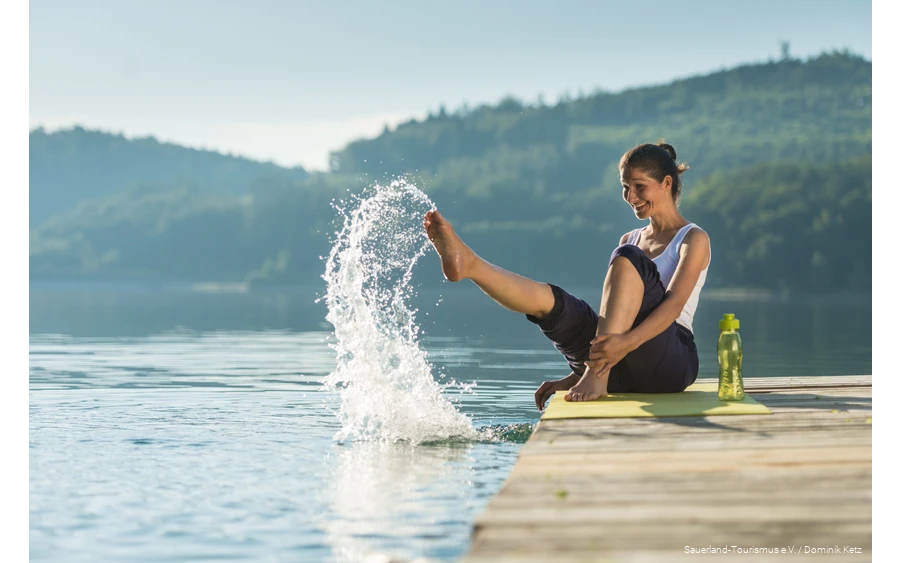 Eine Frau sitzt auf einem Steg am Hennesee und spritzt mit Wasser.