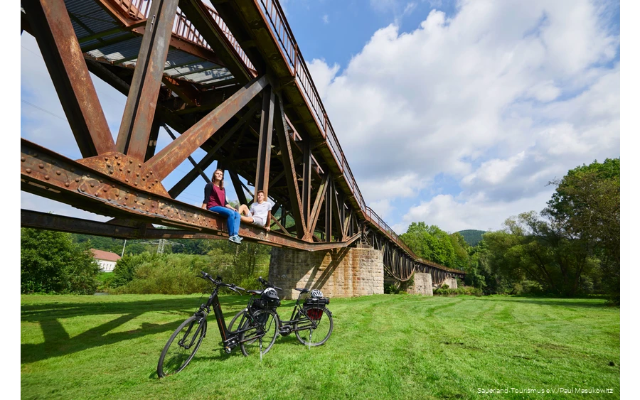 Couple sitting on the girder of a bridge with two e-bikes underneath them