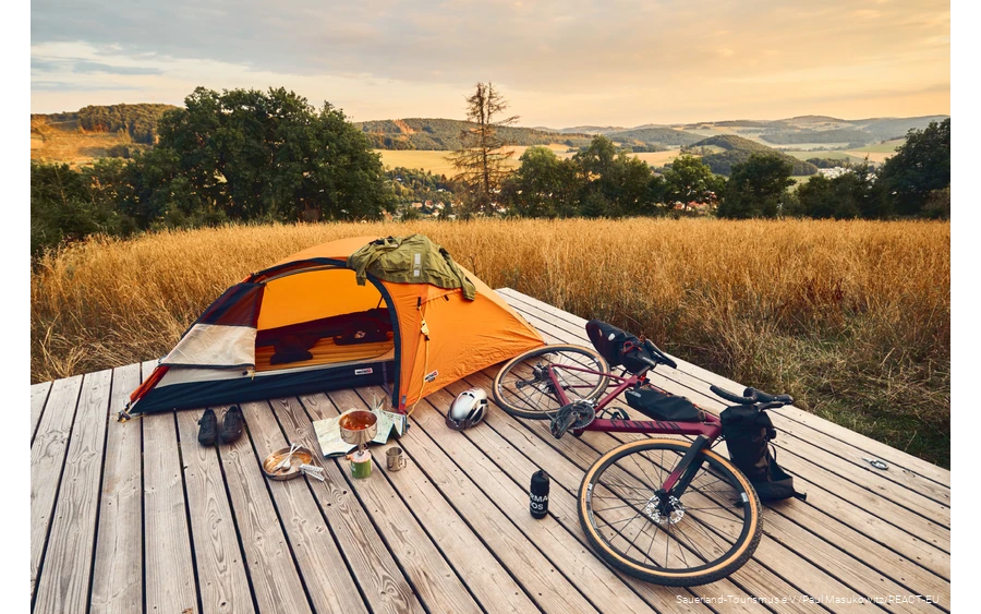 Gravel bike and tent on a trekking platform with a view over the Sauerland landscape