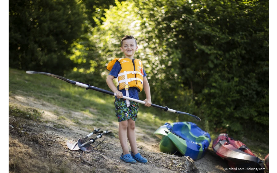 Boy with life jacket looking forward to canoeing with a paddle in his hand.