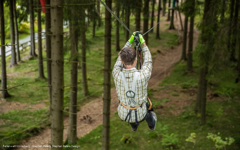 Eine Person fliegt an einem Gurt und Seil gesichert von einem Baum zum nächsten.