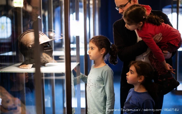 Een vader en drie dochters staan voor een vitrine in een museum. Ze kijken naar een ridderhelm.