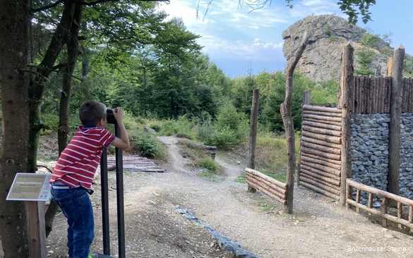 Ein Junge steht am Wall der Bruchhauser Steine und schaut durch ein fest montiertes Fernglas zum Feldstein.