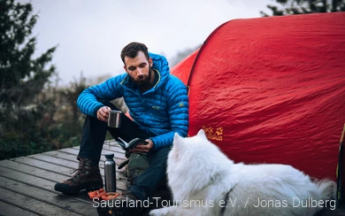 Ein Mann übernachtet mit seinem Hund auf einem Trekkingplatz