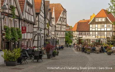 Ein Platz in Soest mit lauter Fachwerkhäusern und Menschen, die draußen in Gaststätten sitzen