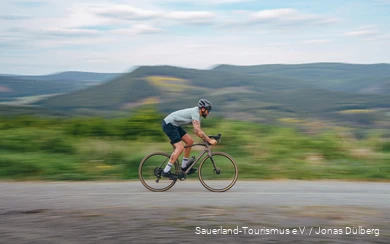 Tätowierter Mann auf einem Gravelbike im Profil. Die Umgebung ist verschwommen.