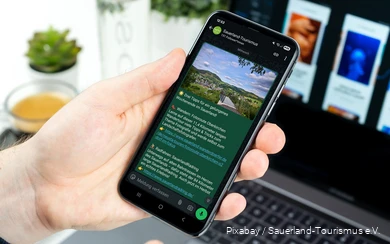 Ein Smartphone wird in der Hand gehalten. Auf dem Bildschirm sieht man einen Post im neuen WhatsApp-Kanal des Sauerland-Tourismus.