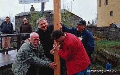 Vier Männer stellen erfreut den ersten Wegweiser des Rothaarsteigs im Rahmen seiner Eröffnung auf. Auf dem Schild sind die Distanzen zu den beiden Start-/Endpunkten des Fernwanderwegs zu sehen.