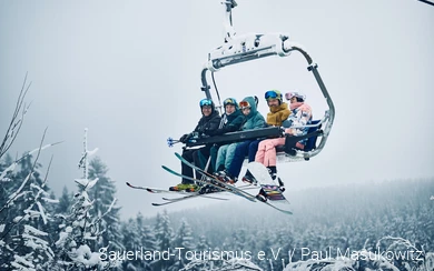 Eine fröhliche Gruppe Wintersportler sitzt im Sessellift.