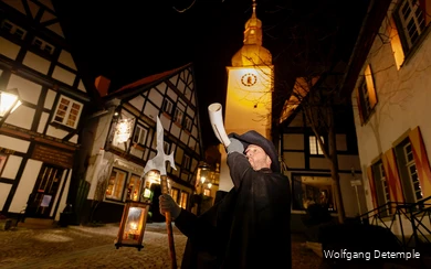 Ein als Nachtwächter verkleideter Mann steht in der Arnsberger Altstadt und bläst ein Horn.
