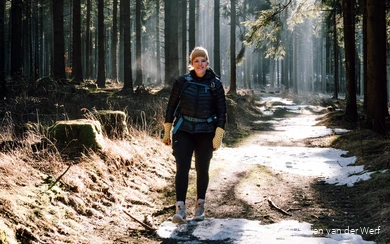 Bloggerin Paulien wandert durch einen Fichtenwald mit kleinen Flecken von Schnee auf dem Waldweg.