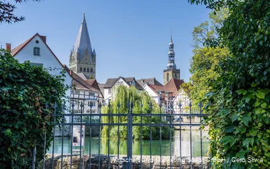 op de voorgrond is een vijver in het centrum van Soest, op de achtergrond zie je vakwerkhuizen en twee kerktorens onder een helderblauwe hemel in de zomer