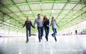 Vater, Mutter und zwei Töchter fahren Hand-in-Hand auf Schlittschuhen.