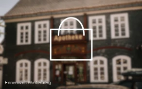 Verschwommenes Bild einer Apotheke mit der Zeichnung eines Koffers im Vordergrund. Dieses Bild dient als Symbolbild für Apotheken.