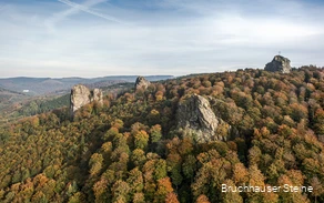 Luftaufnahme der Bruchhauser Steine, die zwischen herbstlich verfärbtem Laub hervorragen. Auf dem rechten Stein steht ein Gipfelkreuz.
