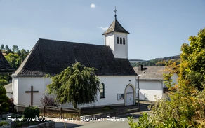 Eine Kirche vor blauem Himmel und einem Baum im Vordergrund.
