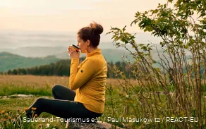A hiker enjoys her break with a cup of coffee and a view over the landscape.