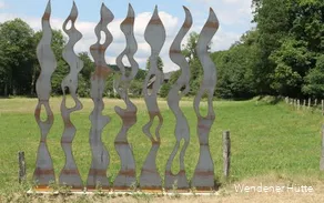 rostende Metallstelen in Form von Feuerflammen auf einer Wiese