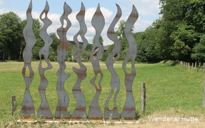 rostende Metallstelen in Form von Feuerflammen auf einer Wiese