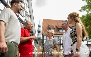 Einblick in eine Stadtführung in Soest mit einem Guide in rotem T-Shirt. Im Hintergrund sind eine der zahlreichen Soester Kirchen und Fachwerkhäuser zu sehen.