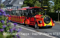 Eine rot-gelbe Eisenbahn fährt die Straße entlang.