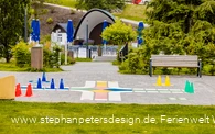 Im Vordergrund ein großes, ins Pflaster integriertes, Mensch ärgere dich nicht Spiel mit der Musikmuschel im Hintergrund.