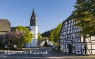 Eine Kirche an einer Straße mit einem Fachwerkhaus im Vordergrund.