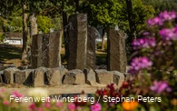 Ein steinerner Brunnen mit vier großen Steinsäulen, aus denen Wasser sprudelt.