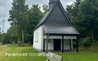Bank vor einer Kapelle, welche von Bäumen umgeben wird.