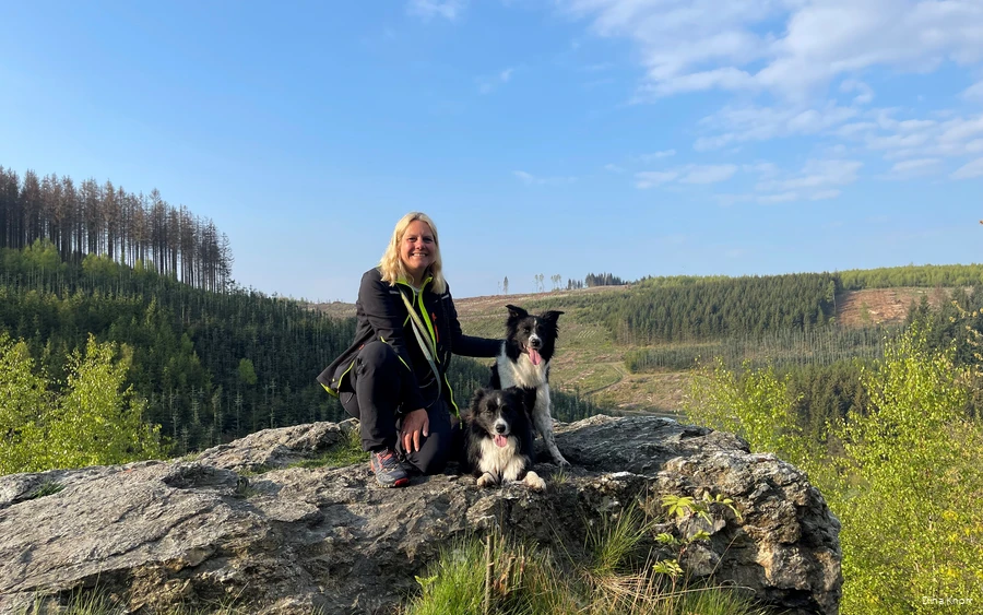 Blogger Dina Knorr poseert met haar twee honden tegen de achtergrond van het groene landschap van het Sauerland tijdens een van haar wandeltochten.