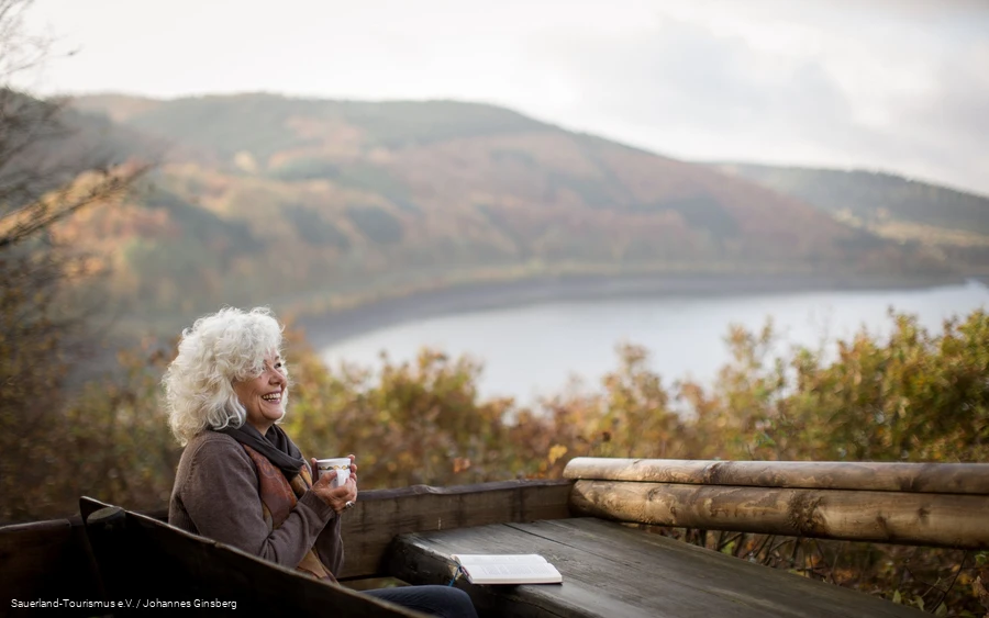 A woman relaxes while reading in the fall landscape around the Biggesee.