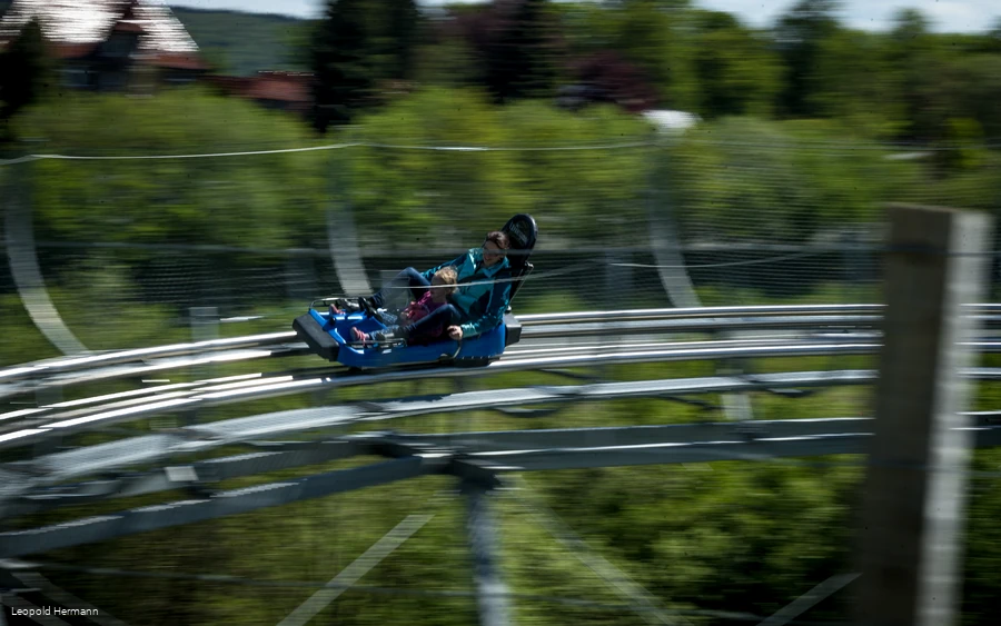 Eine Mutter mit Kind fährt auf einem Rodelschlitten durch eine Kurve auf einer Sommerrodelbahn.