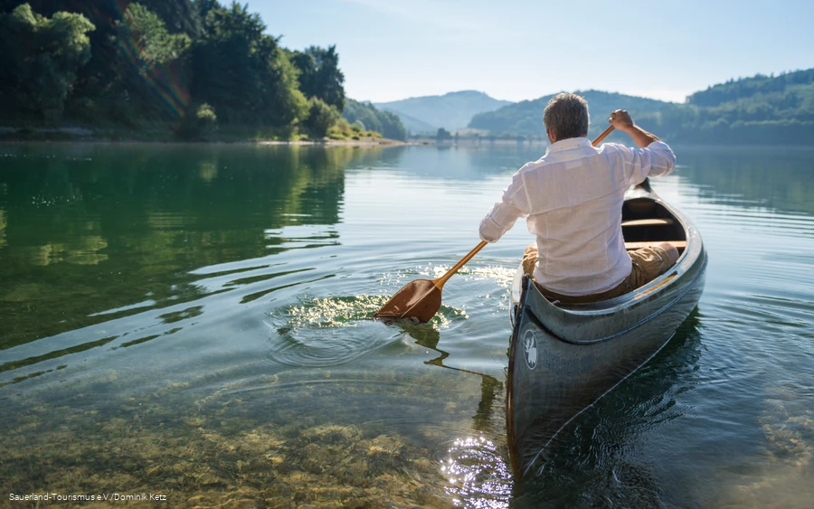 Een man in een wit shirt zit in een kano op de Hennesee en de zon wordt weerspiegeld in het water