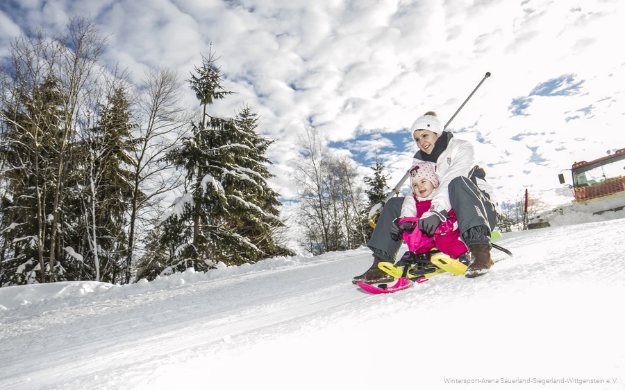 Woman riding down the slope with her child on a sledge.